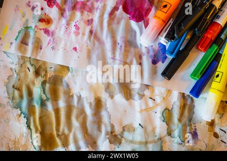 Vue de dessus de stylos aquarelles multicolores avec des capuchons torsfiables placés sur des feuilles blanches tachées et froissées pendant les travaux de peinture à la lumière du jour Banque D'Images