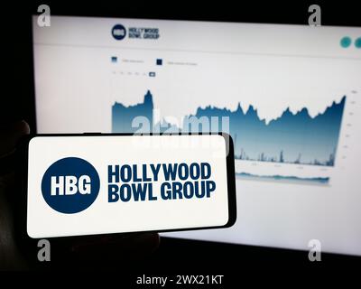 Personne tenant le téléphone portable avec le logo de la société de bowling britannique Hollywood Bowl Group plc devant la page Web de l'entreprise. Concentrez-vous sur l'affichage du téléphone. Banque D'Images