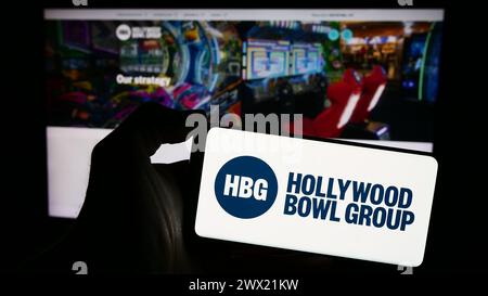 Personne tenant un smartphone avec le logo de la société de bowling britannique Hollywood Bowl Group plc en face du site Web. Concentrez-vous sur l'affichage du téléphone. Banque D'Images