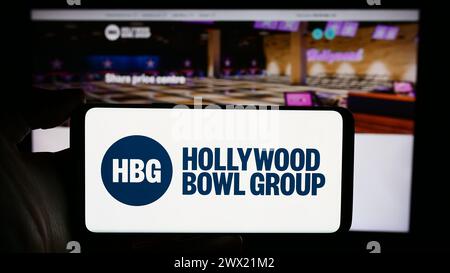 Personne tenant le téléphone portable avec le logo de la société de bowling britannique Hollywood Bowl Group plc devant la page Web de l'entreprise. Concentrez-vous sur l'affichage du téléphone. Banque D'Images