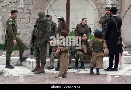 Des enfants israéliens en costume militaire se tiennent au milieu des membres des forces de sécurité israéliennes alors que les colons juifs défilent lors de la parade annuelle de Pourim le 24 mars 2024 à Hébron, en Israël. Banque D'Images