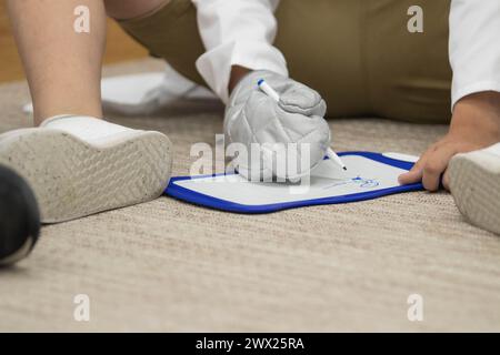 Gros plan d'un enfant assis à la salle de classe, jouant. L'enfant dessine sur un tableau blanc avec un sharpie tout en portant un gant de four Banque D'Images