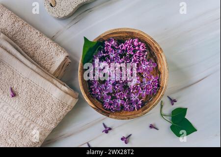 Spa et composition de bien-être avec de l'eau de fleurs de lilas parfumées dans un bol en bois et des serviettes éponge sur fond de marbre, aromathérapie, vue de dessus, pose à plat. Banque D'Images