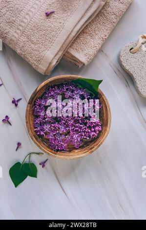 Spa et composition de bien-être avec de l'eau de fleurs de lilas parfumées dans un bol en bois et des serviettes éponge sur fond de marbre, aromathérapie, vue de dessus, pose à plat. Banque D'Images