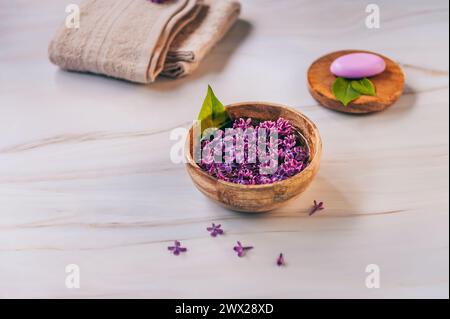 Spa et composition de bien-être avec de l'eau de fleurs de lilas parfumées dans un bol en bois, serviettes éponge et savon fait à la main sur fond de marbre. Banque D'Images