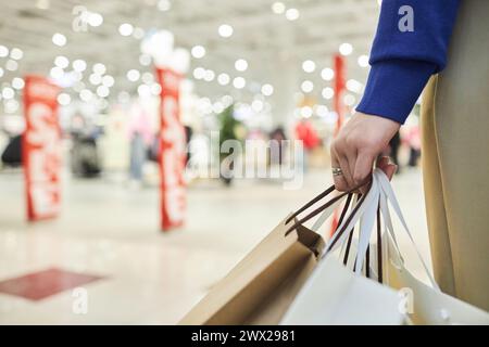 Gros plan extrême d'une main féminine tenant des sacs à provisions debout dans l'espace de copie intérieur du centre commercial Banque D'Images