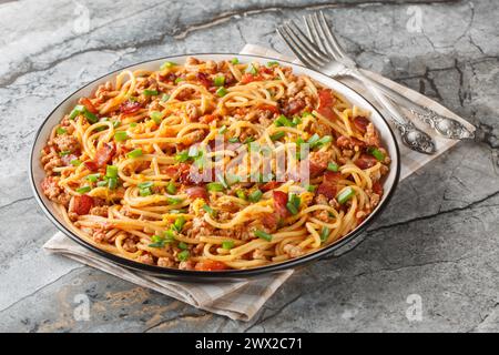 Spaghettis américains avec bacon, viande hachée, fromage cheddar et sauce tomate épicée gros plan dans une assiette sur la table. Horizontal Banque D'Images