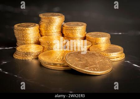 Vue rapprochée piles de pièces Louis dorées et américaines sur une surface en marbre noir et blanc Banque D'Images