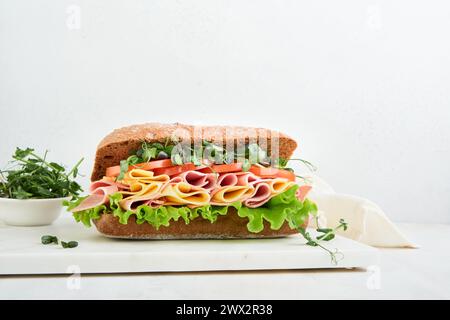 Sandwich. Un grand sandwich sous-marin frais avec jambon, fromage, laitue, tomates et microgreens sur fond clair. Concept de thème du petit déjeuner sain, s Banque D'Images