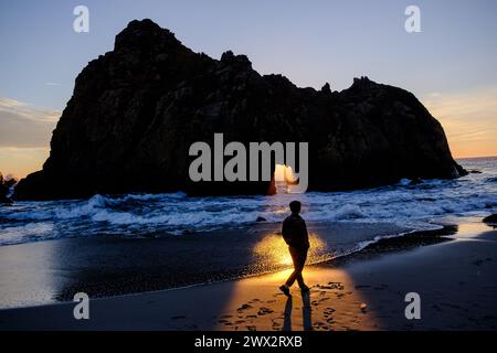 Le coucher de soleil illumine la personne devant la fenêtre dans le Rock caractéristique de Keyhole Arch à Pfeiffer Beach à Big sur sur sur l'océan Pacifique en Californie, États-Unis. Banque D'Images