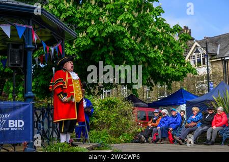 Crieur de ville masculin et chasseur (vêtements de livrée rouge or) faisant une proclamation publique bruyante et bruyante - Ilkley, West Yorkshire, Angleterre Royaume-Uni. Banque D'Images