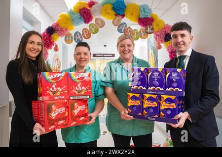 Gloucester, Royaume-Uni. 27 mars 2023. Le Property Centre, un agent immobilier avec des succursales situées à Gloucester, Cheltenham, Stroud et Worcester, a fait don de 52 œufs de Pâques au Centre pour enfants du Gloucestershire Royal Hospital, un pour chaque lit de l'unité. Josh Richards, directeur principal de la succursale du Property Centre - Churchdown (à droite) et Jenna Cebryk, directrice des médias sociaux du Property Centre (à gauche) avec Michelle Wallace et Natalie Hill, spécialistes du jeu au Gloucestershire Royal Hospital. Crédit : Carl Hewlett/Alamy Live News Banque D'Images