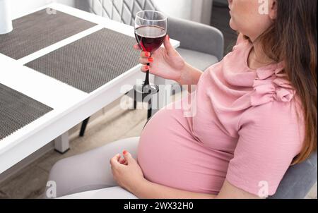 Une fille enceinte avec un gros ventre dans un chemisier rose tient un verre de vin. Le concept de boire de l'alcool pendant la grossesse, une mauvaise habitude. Banque D'Images