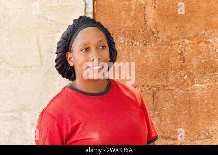 jeune femme africaine célibataire avec des couvre-chefs debout devant la maison dans un village, Banque D'Images