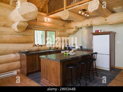 Île avec comptoir en granit gris foncé et tabourets de bar en bois teinté noir dans la cuisine avec sol en carreaux de céramique à l'intérieur de pin blanc oriental fabriqué à la main Banque D'Images