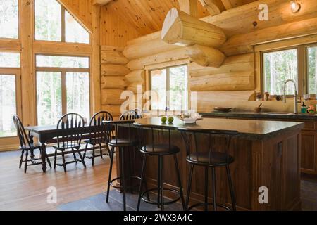 Île avec comptoir en granit gris foncé et tabourets de bar en bois teinté noir plus table en bois antique avec chaises à dossier haut arrondi en concept ouvert Banque D'Images