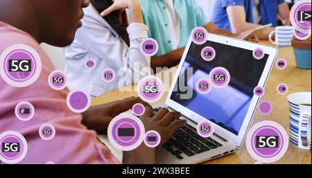 Image de texte 5g avec des symboles sur l'homme afro-américain travaillant sur ordinateur portable dans le bureau. Composite numérique, exposition multiple, entreprise, télécommunication Banque D'Images