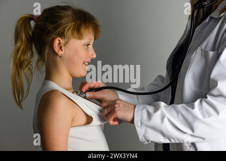 un médecin en manteau blanc avec un stéthoscope écoute les battements de cœur d'une petite fille. Banque D'Images