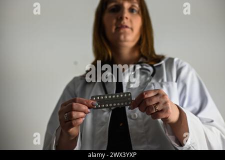 un médecin dans un manteau blanc avec un stéthoscope tient des pilules contraceptives dans sa main, fond flou. Banque D'Images