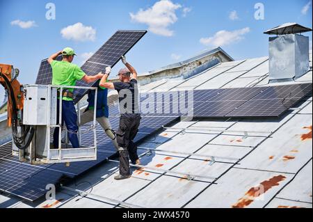 Travailleurs soulevant le panneau solaire photovoltaïque sur le toit métallique de la maison avec l'aide d'un ascenseur de grue. Hommes installateurs installant des modules solaires photovoltaïques à l'extérieur. Concept de génération d'énergie renouvelable. Banque D'Images