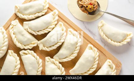 Empanadas argentins crus sur une planche de bois sur une table en marbre. Banque D'Images