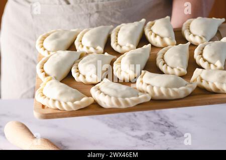 Une main humaine tenant une planche de bois avec des empanadas argentines crues. Banque D'Images