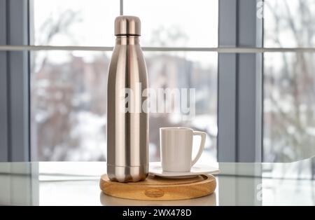 Une bouteille en métal isolée sous vide pour l'eau ou le café et des tasses avec du café sur la table de cuisine. Banque D'Images