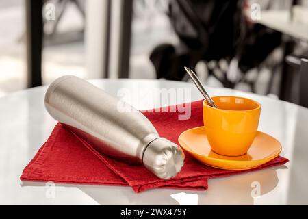 Une bouteille en métal isolée sous vide pour l'eau ou le café et une tasse de café sur une table dans un café. Banque D'Images