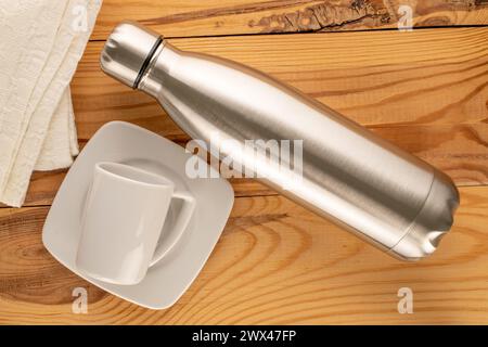 Une bouteille thermos en métal avec tasse en céramique blanche sur table en bois, macro, vue de dessus. Banque D'Images