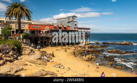 Macabee Beach ou McAbee Beach près de Cannery Row à Monterey, Californie, États-Unis. Touristes à la plage avec un quai et Fish Hopper restaurant. Banque D'Images