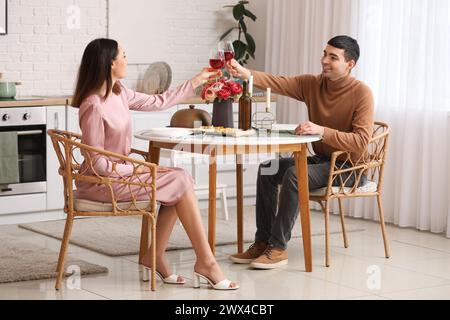 Jeune couple avec des verres de vin assis à la table à manger dans la cuisine Banque D'Images