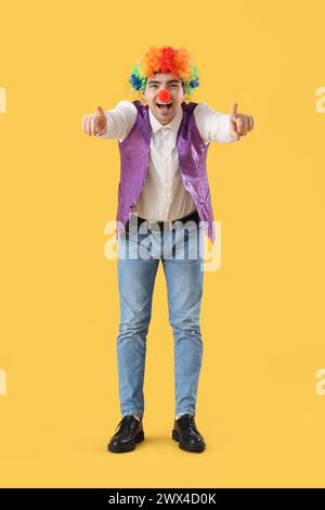 Heureux jeune homme en costume de clown pointant vers le spectateur sur fond jaune Banque D'Images