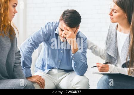 Homme déprimé accro recevant le soutien des membres du groupe lors de la séance de thérapie Banque D'Images