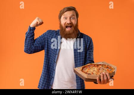 homme barbu aux cheveux roux tenant une boîte à pizza criant en faisant des gestes oui, studio Banque D'Images