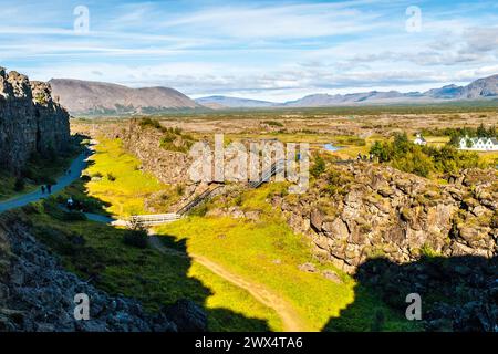 Une vue imprenable sur le fossé géologique du parc national de Thingvellir en Islande, mettant en valeur le paysage distinct marqué par un terrain accidenté et une végétation luxuriante sous un ciel bleu clair. Islande Banque D'Images
