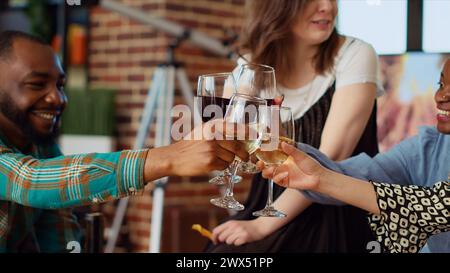 Gros plan de verres à vin grillés à la fête à la maison par un groupe multiethnique de personnes célébrant leur amitié ensemble. Amis ayant des réunions, dégustant des collations de charcuterie Banque D'Images