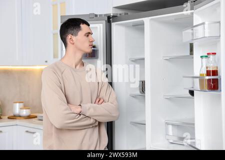 Homme bouleversé près d'un réfrigérateur vide dans la cuisine Banque D'Images