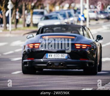 Haguenau, France - 20 mars 2024 : vue floue floue d'une Porsche 911 Carrera GTS noire dans les rues de Haguenau, ses feux arrière uniques brillent lorsqu'elle navigue dans la circulation urbaine Banque D'Images