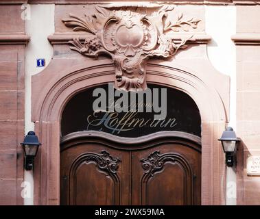 Haguenau, France - 20 mars 2024 : élégante porte en bois ornée de sculptures ornées et d'un signe écrit, nichée dans un cadre de rue européenne pittoresque Banque D'Images