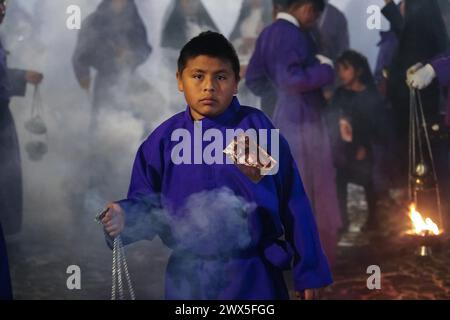 Antigua, Guatemala. 27 mars 2024. Un jeune pénitent utilise un censeur pour répandre de l'encens devant le massif flotteur processionnel Jesús Nazareno del Milagro pendant la traditionnelle Santa Semana célébrant la semaine Sainte, le 27 mars 2024 à Antigua, Guatemala. Les processions opulentes, les algèbres détaillées et les traditions séculaires attirent plus d'un million de personnes dans l'ancienne capitale. Crédit : Richard Ellis/Richard Ellis/Alamy Live News Banque D'Images