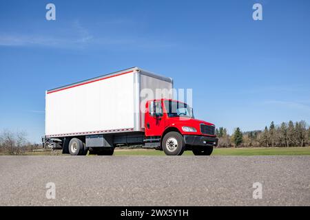 Semi-camion semi-remorque de transporteur industriel de charge moyenne rouge avec remorque de caisse transportant des marchandises conduisant sur la route locale pour la livraison en journée ensoleillée Banque D'Images