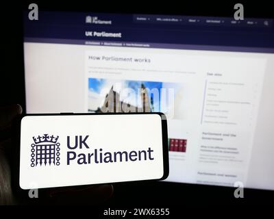 Personne tenant un smartphone avec le logo de l'organe législatif Parlement du Royaume-Uni (UK) devant le site Web. Concentrez-vous sur l'affichage du téléphone. Banque D'Images