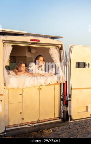Couple assis à l'arrière d'un camping-car, observant le lever du soleil dans un endroit isolé avec une atmosphère sereine. Banque D'Images