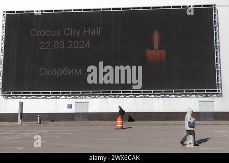 Moscou, Russie. 28 mars 2024. Un piéton passe devant un écran affichant une image en deuil des victimes d'un attentat terroriste près de l'hôtel de ville de Crocus dans la banlieue de Moscou, Russie, le 28 mars 2024. Le nombre de morts de l'attaque terroriste de vendredi a augmenté à 143 après que des hommes armés ont pris d'assaut une salle de concert dans la banlieue de Moscou, selon une liste publiée mercredi par le ministère russe des situations d'urgence. Crédit : Bai Xueqi/Xinhua/Alamy Live News Banque D'Images