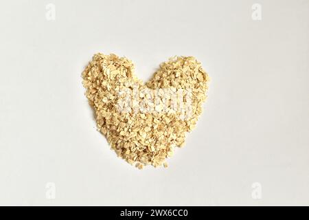 Les flocons d'avoine instantanés sont disposés en forme de coeur sur un fond blanc. Banque D'Images