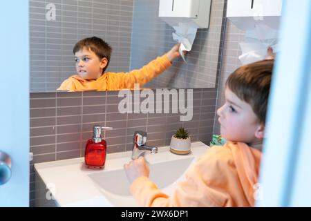 Garçon prenant du papier pour sécher ses mains dans une salle de bain après s'être lavé les mains Banque D'Images