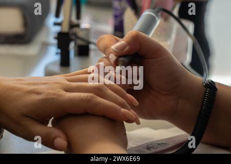 Esthéticienne limant les ongles avec un fileur électrique à une femme dans un centre de beauté Banque D'Images