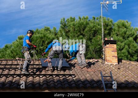 Trois techniciens en installation de panneaux solaires installant des panneaux solaires sur le toit d'une maison Banque D'Images