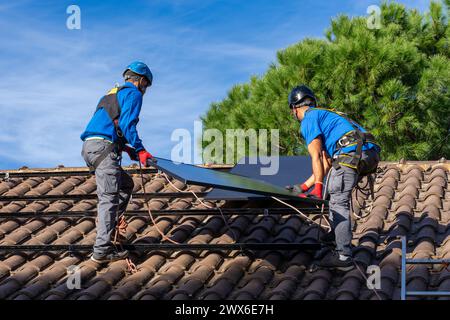 Deux installateurs de panneaux solaires installant des panneaux solaires sur le toit d'une maison Banque D'Images