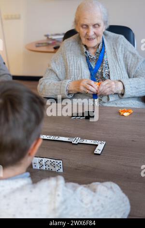 Femme âgée jouant aux dominos avec son arrière-petit-fils tout en mangeant une mandarine Banque D'Images